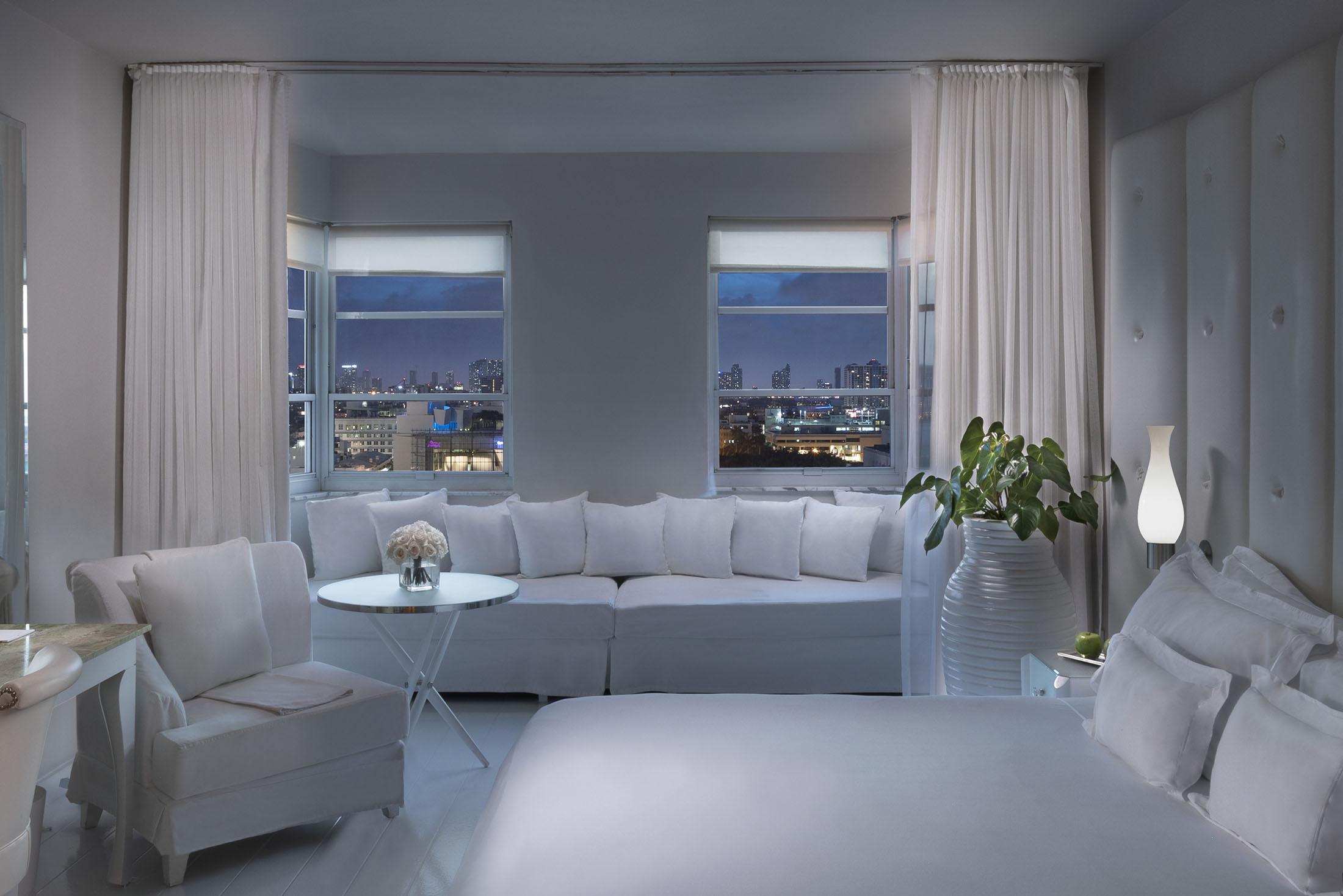 cama branca e alcova de assento branco na frente da janela com vista para a cidade