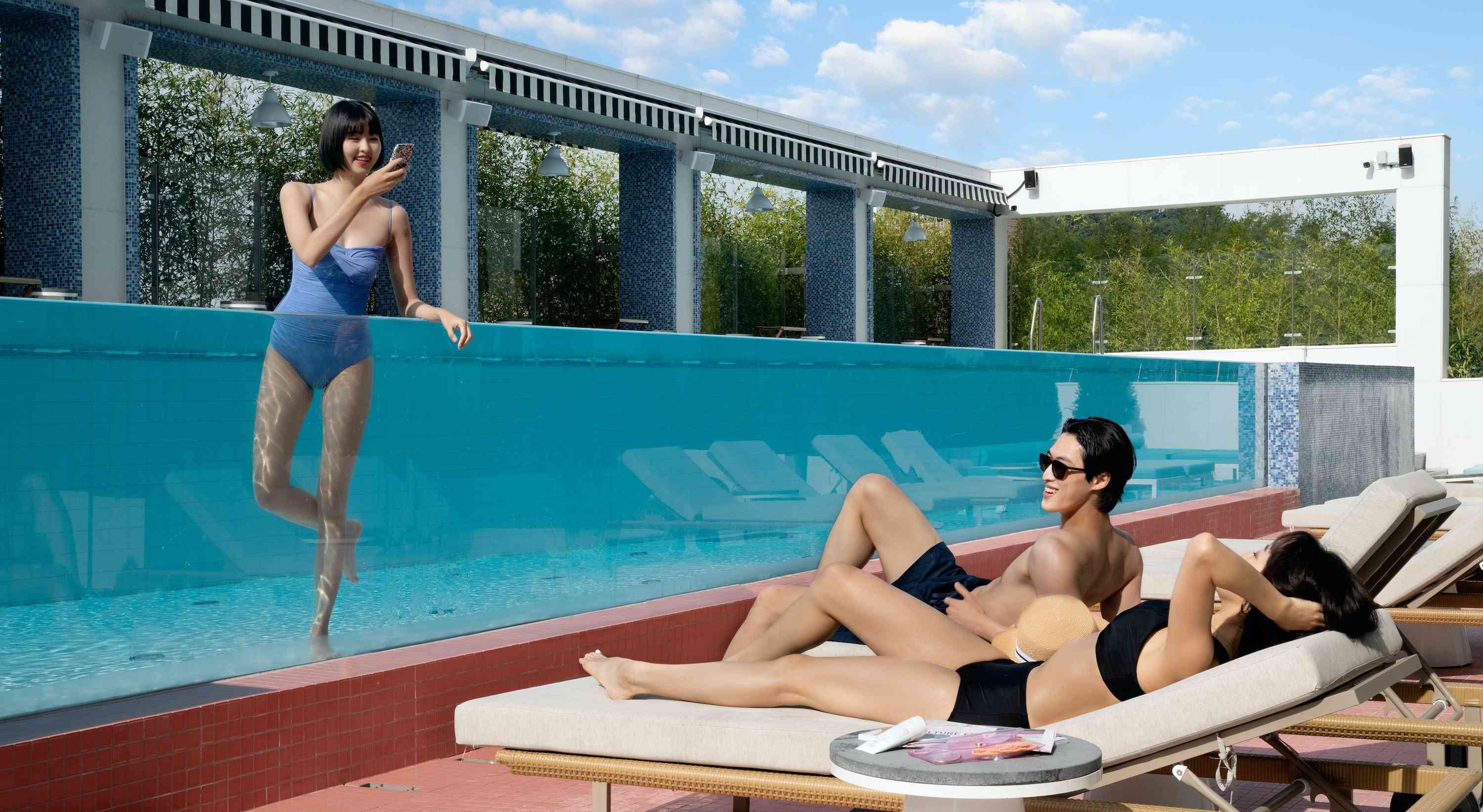 casal nas espreguiçadeiras à beira da piscina com um amigo na piscina