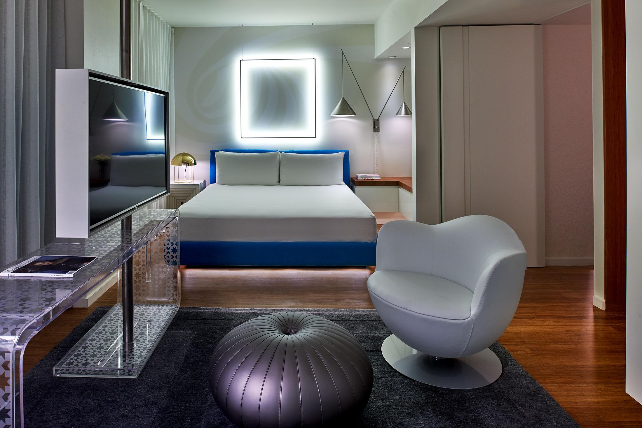 Um quarto de hotel com uma luz quadrada atrás da cama e uma cadeira em primeiro plano.